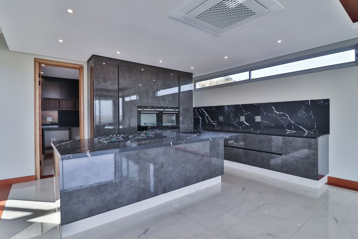 Modern kitchen featuring high-gloss cabinetry, marble-look countertops, integrated oven and hob, and a convenient adjoining scullery area.