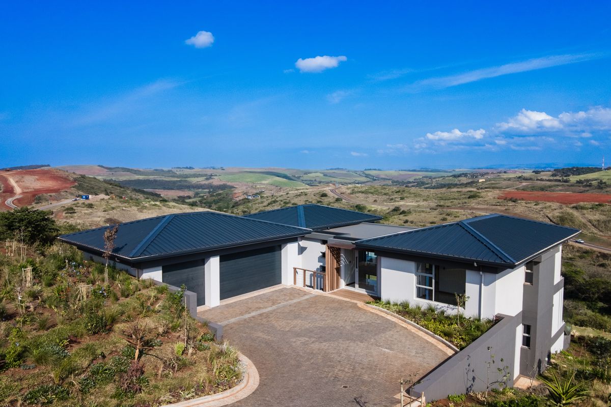 Aerial view of a modern single-story residence featuring a dark metal roof, paved driveway, double garage, and landscaped surroundings with expansive rural views.