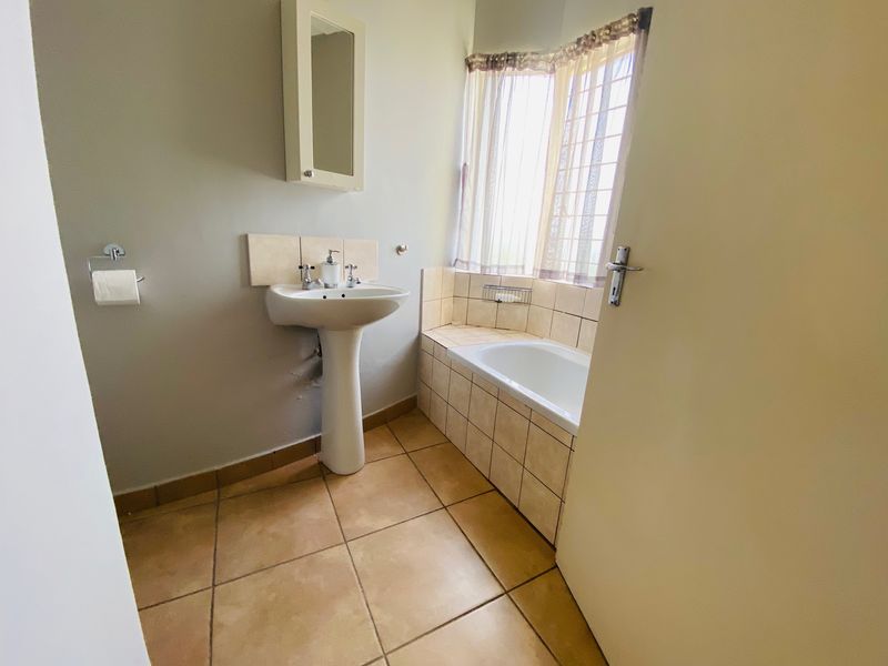A functional bathroom featuring a pedestal basin, built-in bathtub with tiled surround, and neutral floor tiling, offering a clean and practical space.