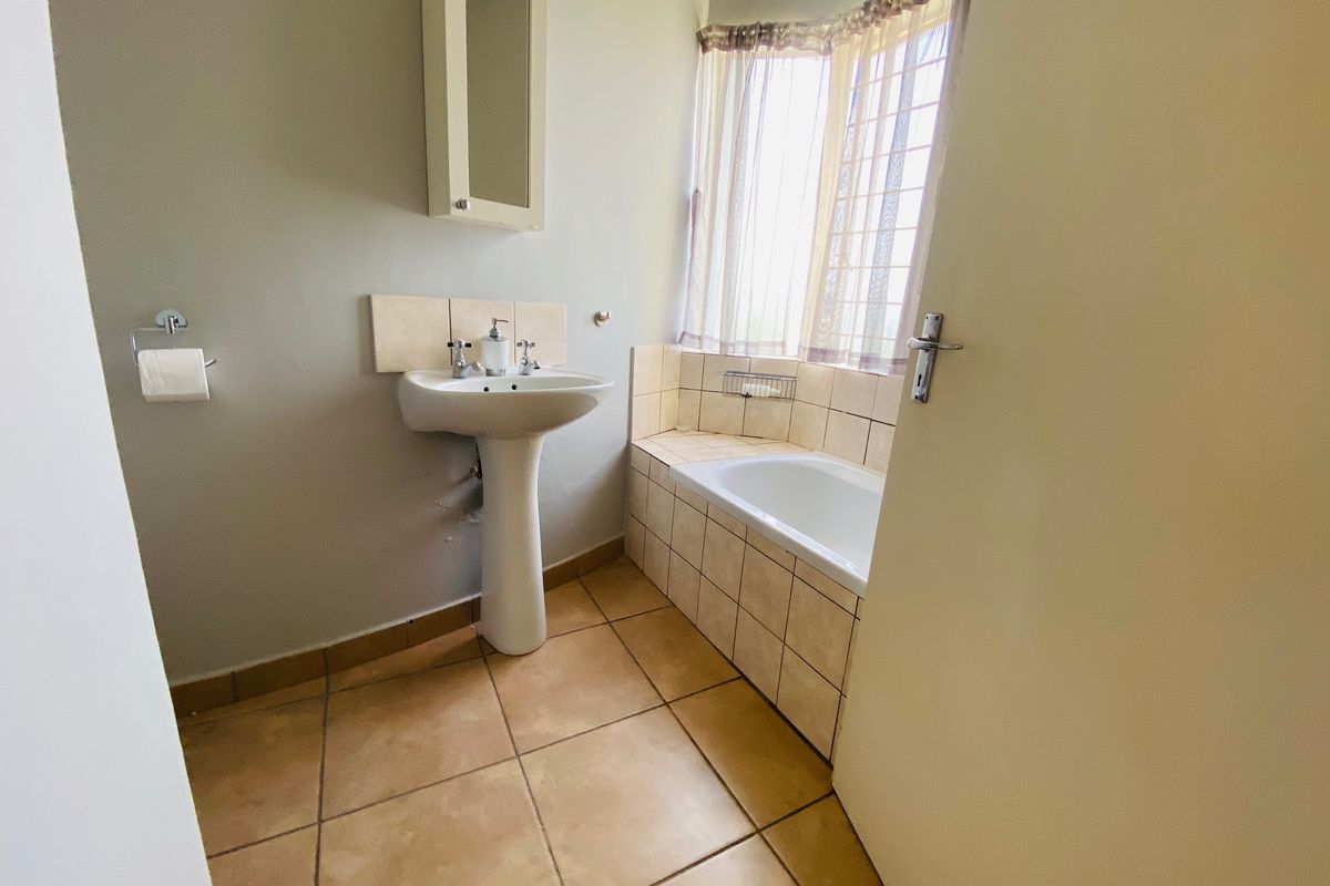 A functional bathroom featuring a pedestal basin, built-in bathtub with tiled surround, and neutral floor tiling, offering a clean and practical space.