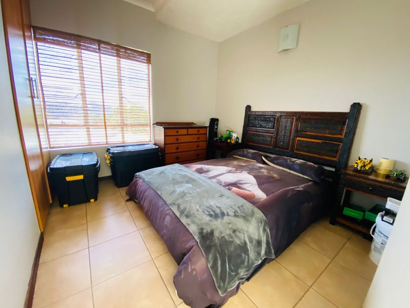 A bedroom featuring tiled flooring, a built-in wardrobe, and venetian blinds, providing a functional space with neutral wall finishes.