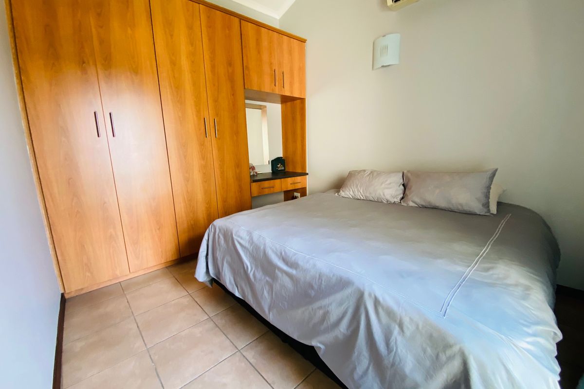 A bedroom featuring built-in wooden cupboards with an integrated vanity, tiled flooring, and a wall-mounted air conditioning unit.