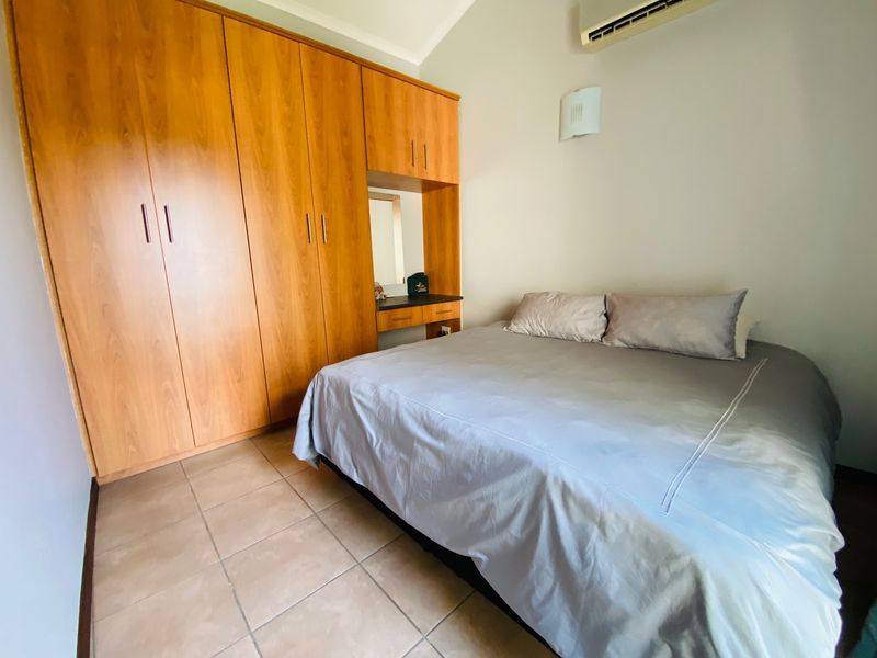 A bedroom featuring built-in wooden cupboards with an integrated vanity, tiled flooring, and a wall-mounted air conditioning unit.