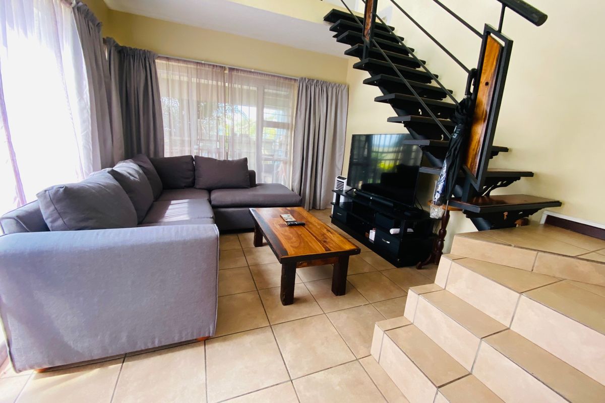 Open-plan living area featuring tiled flooring and a prominent metal staircase leading to the upper level, with access to an outdoor patio.
