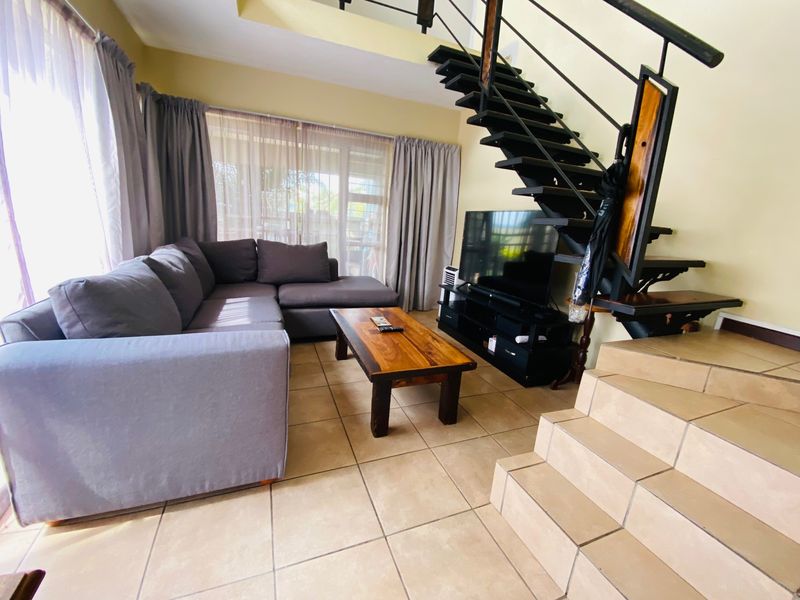Open-plan living area featuring tiled flooring and a prominent metal staircase leading to the upper level, with access to an outdoor patio.