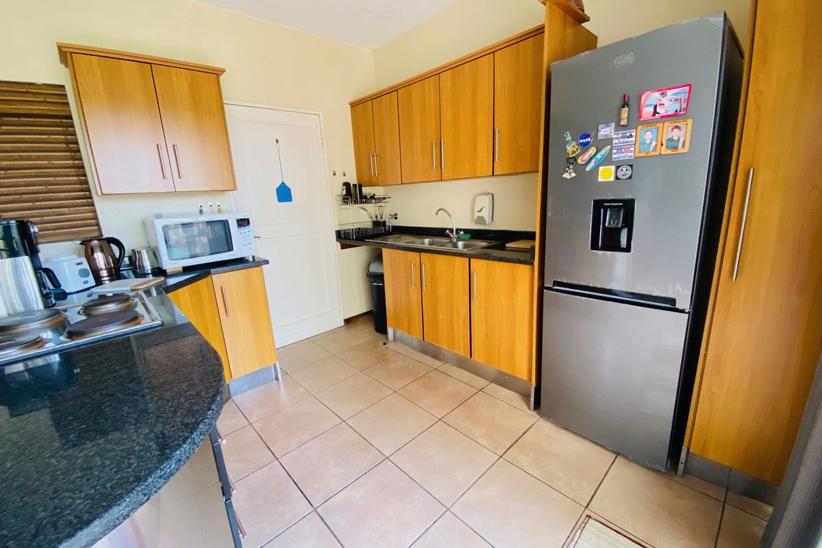 A functional kitchen featuring wooden cabinetry, granite countertops, and tiled flooring, providing a practical workspace with integrated sink and hob.