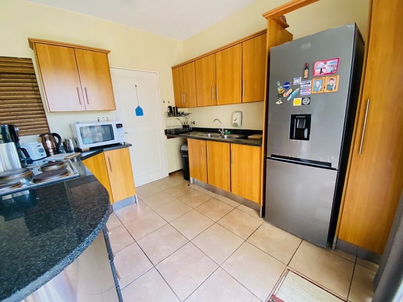 A functional kitchen featuring wooden cabinetry, granite countertops, and tiled flooring, providing a practical workspace with integrated sink and hob.