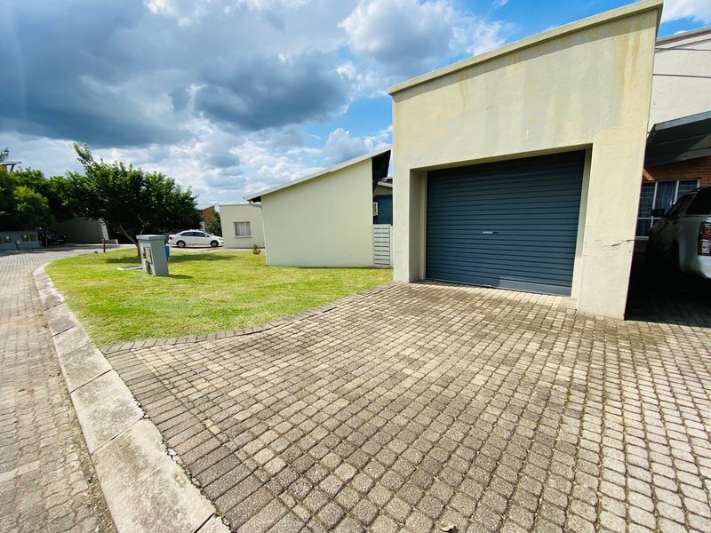 Front exterior view of the apartment featuring a paved driveway, a single roller garage door, and a well-maintained lawn area.