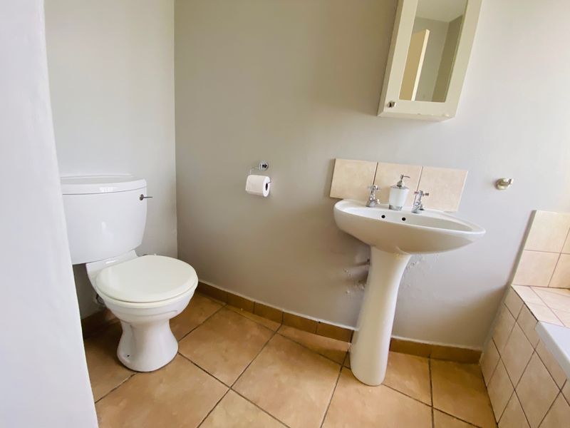 A functional bathroom featuring a pedestal basin, toilet, and tiled flooring, requiring minor cosmetic repairs to the wall finish.