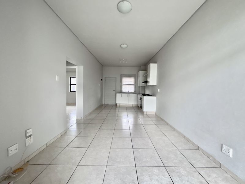 An open-plan living and kitchen area featuring neutral tiled flooring, built-in cabinetry, and a functional kitchen layout with integrated appliances.