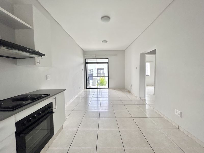 An open-plan kitchen and living area featuring tiled flooring, a built-in oven with gas hob, and access to a balcony through a sliding glass door.