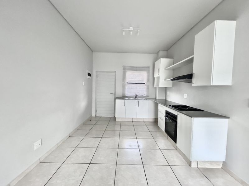 A clean, modern kitchen featuring white built-in cabinetry, a built-in oven and hob, extractor fan, and neutral tiled flooring.