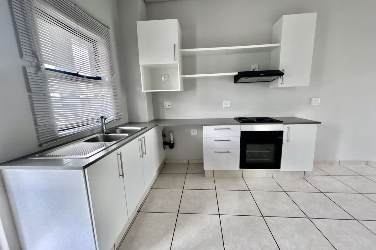 A clean, modern kitchen featuring white cabinetry, stainless steel sink, built-in oven, gas hob, extractor fan, and neutral tiled flooring.