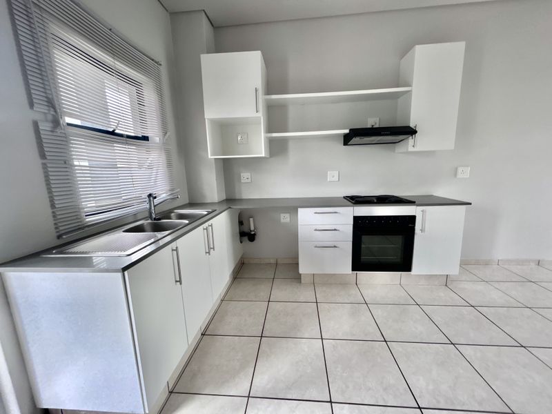 A clean, modern kitchen featuring white cabinetry, stainless steel sink, built-in oven, gas hob, extractor fan, and neutral tiled flooring.