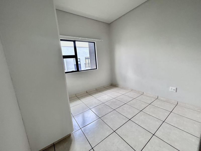 A clean, empty bedroom featuring neutral tiled flooring and a modern aluminium-framed window, providing a blank canvas for interior design.