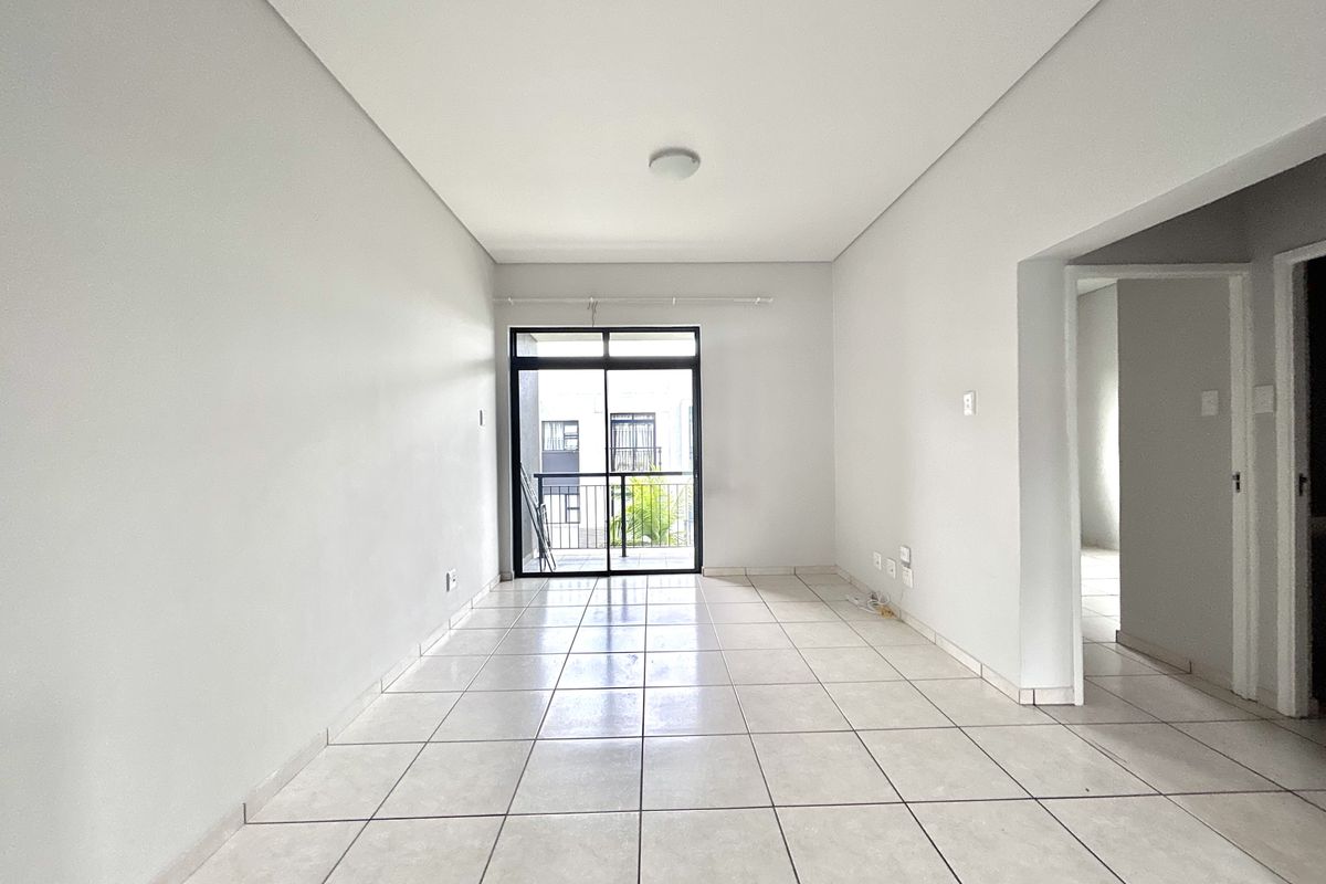 A bright, empty living room featuring neutral tiled flooring and a sliding glass door providing access to a private balcony.