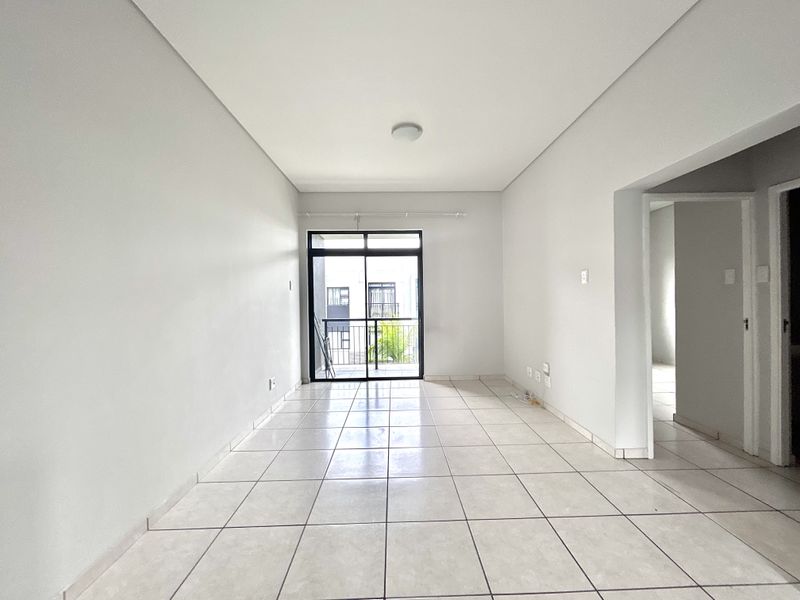 A bright, empty living room featuring neutral tiled flooring and a sliding glass door providing access to a private balcony.