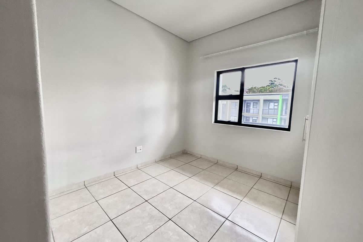 A clean, empty bedroom featuring neutral tiled flooring and a modern black-framed window, providing a blank canvas for personalization.