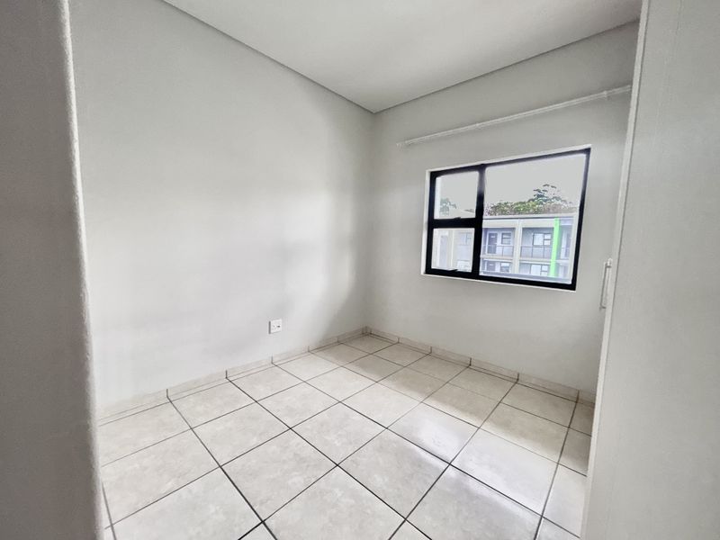 A clean, empty bedroom featuring neutral tiled flooring and a modern black-framed window, providing a blank canvas for personalization.