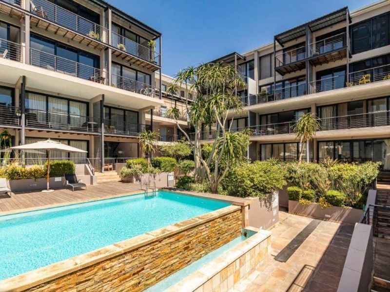 A well-maintained communal pool area featuring stone-clad water features, timber decking, and landscaped gardens surrounded by modern apartment balconies.