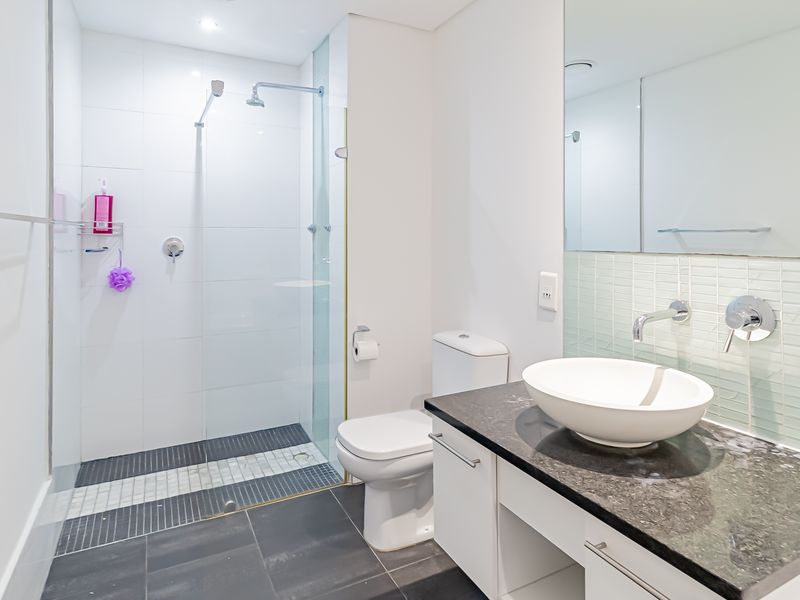 Modern bathroom featuring a walk-in shower with glass screen, a sleek vanity with stone countertop, vessel sink, and a large wall mirror.