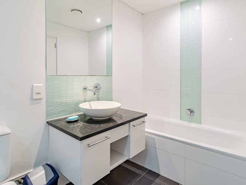 Modern bathroom featuring a stone-topped vanity with a vessel sink, wall-mounted faucet, and a clean built-in bathtub with tiled accents.