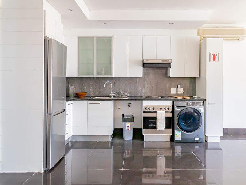 A clean, modern kitchen featuring white cabinetry, dark tiled flooring, integrated appliances, and a sleek grey backsplash, offering a functional and minimalist cooking space.