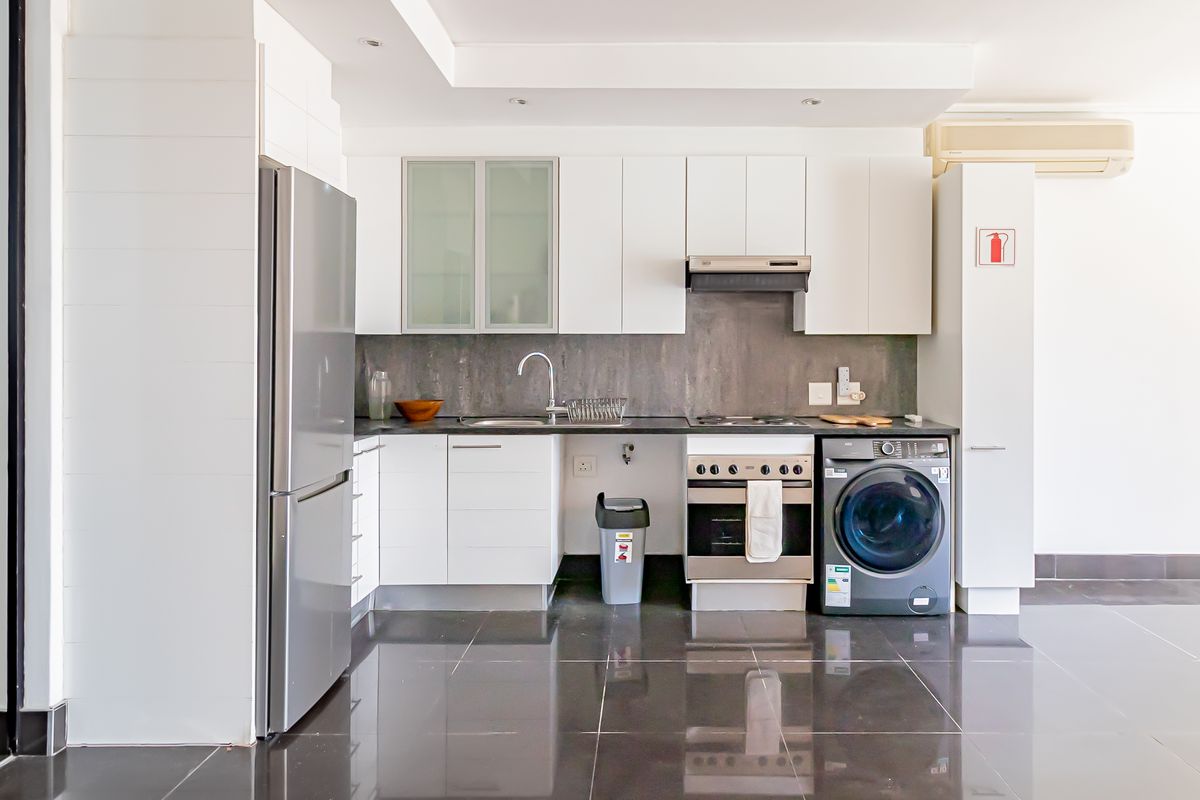 A clean, modern kitchen featuring white cabinetry, dark tiled flooring, integrated appliances, and a sleek grey backsplash, offering a functional and minimalist cooking space.