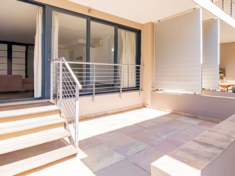 A well-maintained private patio featuring stone tile flooring, a modern metal balustrade, and adjustable privacy shutters, providing seamless indoor-outdoor flow.