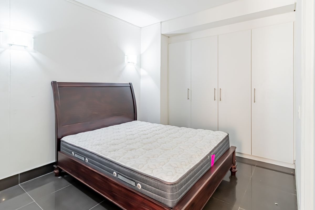 A bright bedroom featuring dark tiled flooring, built-in white cupboards, and modern wall-mounted lighting.