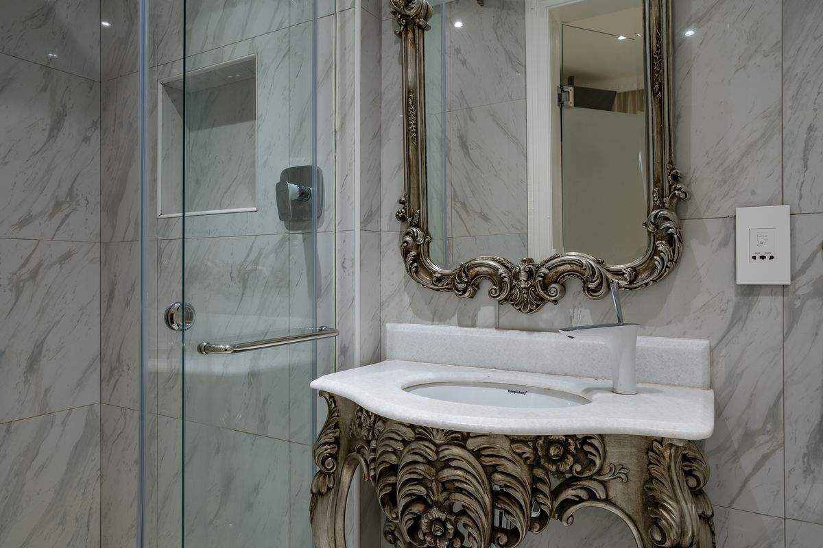 Modern bathroom featuring marble-effect wall tiling, a glass-enclosed shower with a built-in niche, and a decorative vanity unit with a stone countertop.
