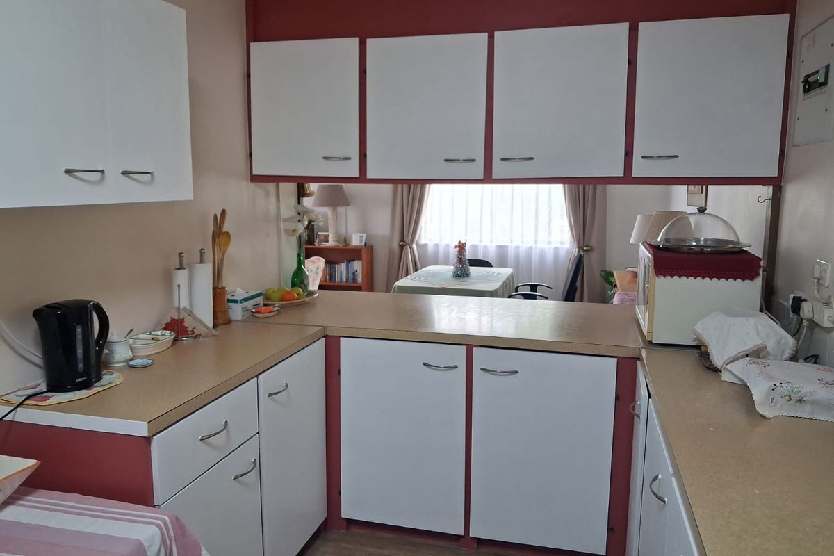 A compact kitchen featuring dated white cabinetry, laminate countertops, and a functional layout with a pass-through opening to the adjacent dining area.