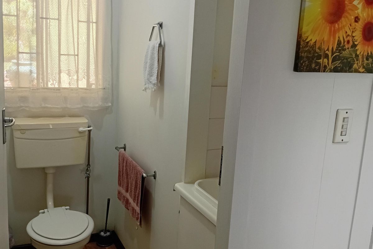 A functional bathroom featuring a standard toilet, a small built-in washbasin, and wood-look flooring with natural light from a window.