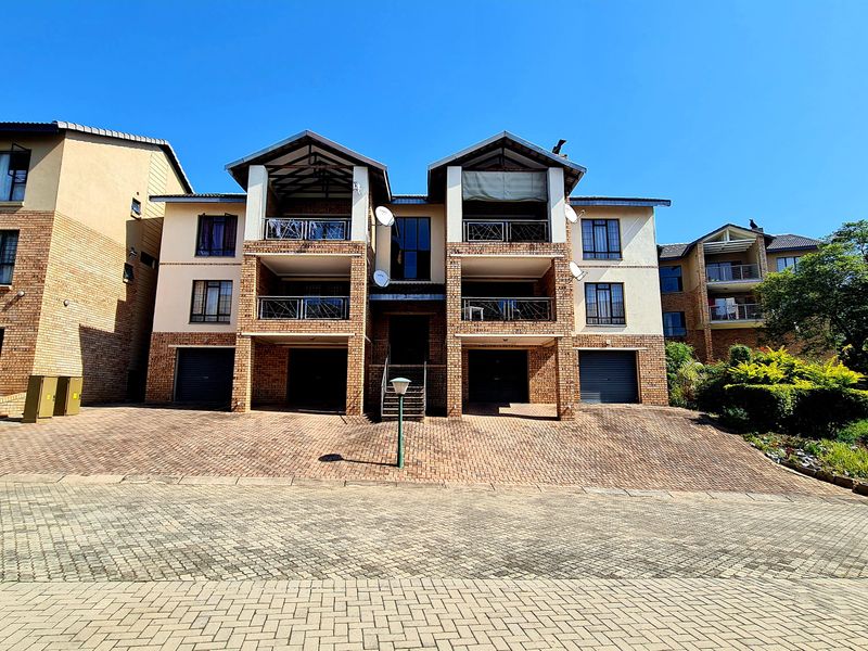 Front elevation of a multi-story apartment complex featuring brick facade, integrated garages, and private balconies under a clear blue sky.