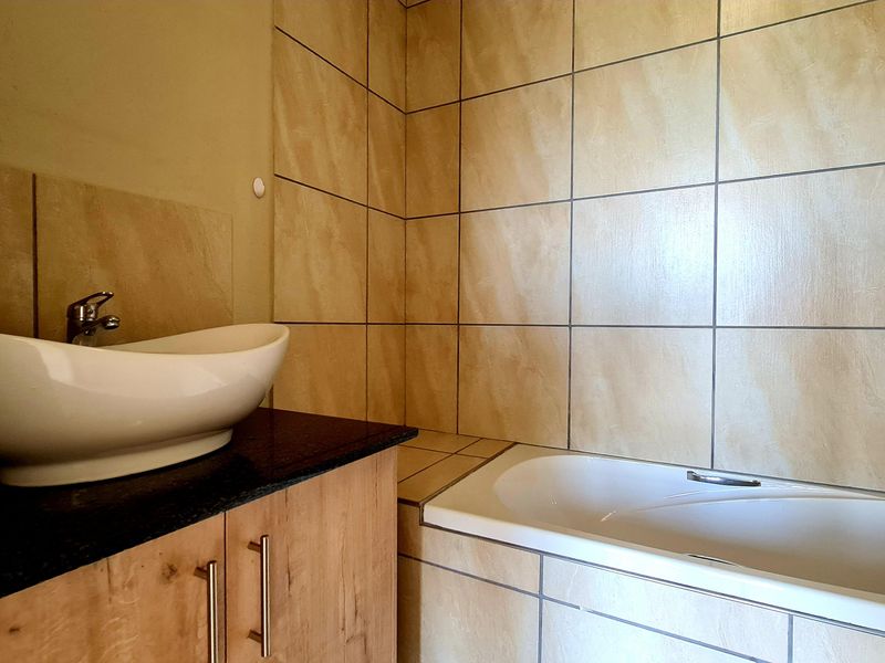 A clean bathroom featuring a modern vessel sink on a vanity cabinet with a granite countertop and a built-in bathtub with tiled surround.