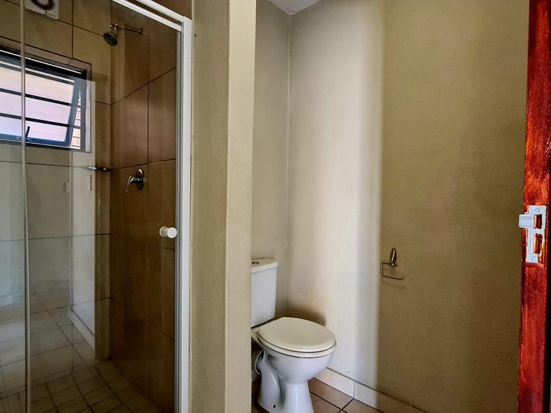A functional bathroom featuring a tiled shower enclosure and a separate toilet area with neutral wall finishes.