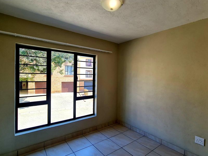 An empty bedroom featuring tiled flooring, a window with security bars, and neutral wall finishes, offering a blank canvas for personalization.