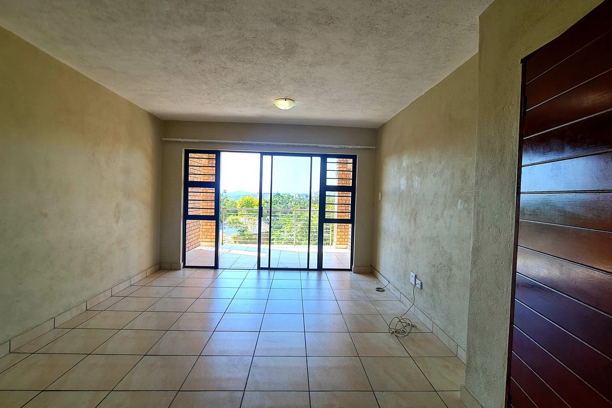 An empty, tiled living room featuring a sliding glass door that opens onto a balcony with scenic views.