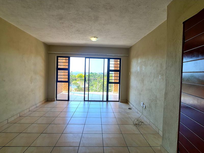An empty, tiled living room featuring a sliding glass door that opens onto a balcony with scenic views.