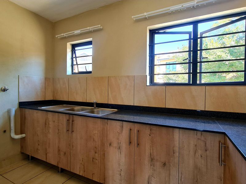 A functional kitchen featuring wood-look cabinetry, granite countertops, a stainless steel sink, and tiled splashbacks with security-fitted windows.