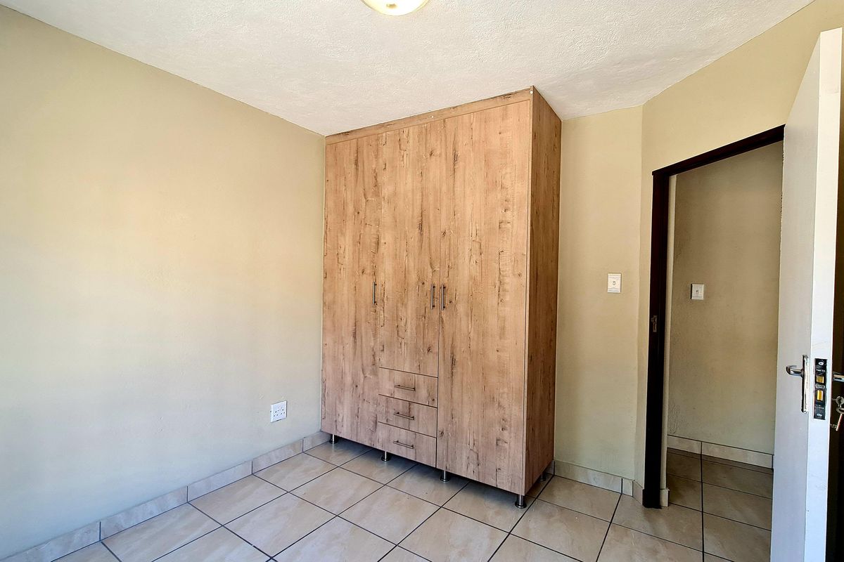 A clean, empty bedroom featuring neutral wall tones, tiled flooring, and a modern wood-finish built-in wardrobe.