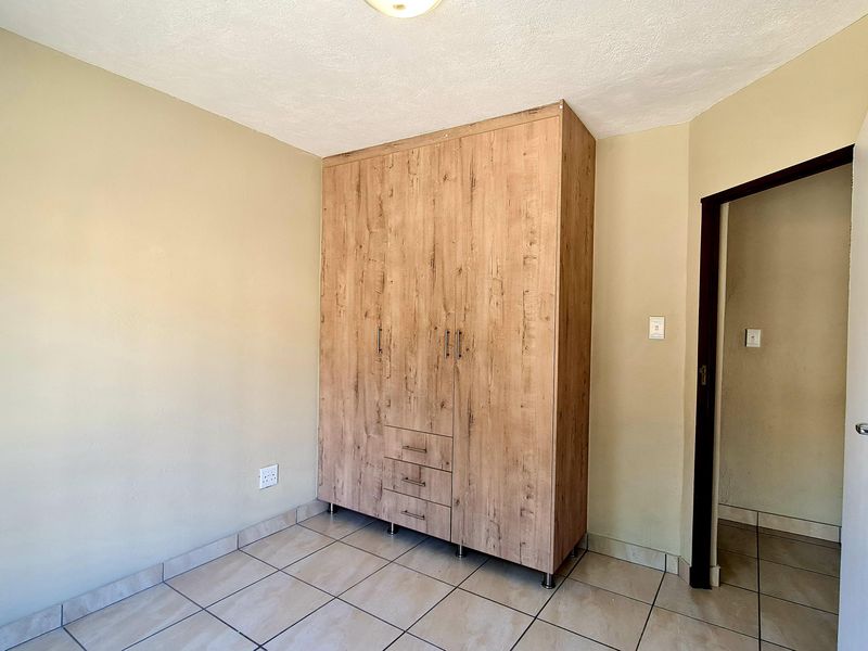 A clean, empty bedroom featuring neutral wall tones, tiled flooring, and a modern wood-finish built-in wardrobe.