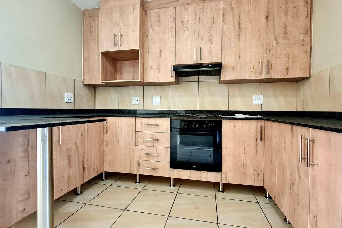 A clean, modern kitchen featuring light wood-finish cabinetry, dark granite countertops, a built-in oven, and a tiled backsplash.
