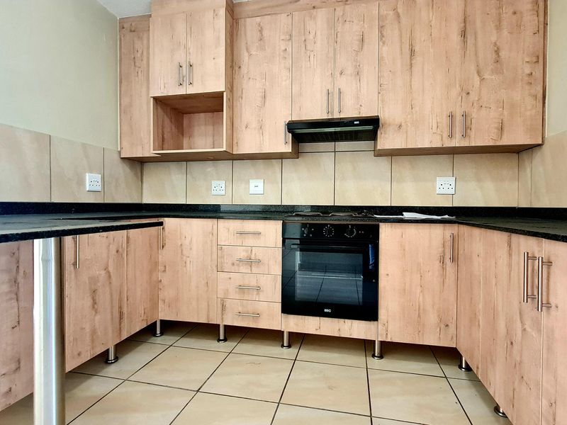 A clean, modern kitchen featuring light wood-finish cabinetry, dark granite countertops, a built-in oven, and a tiled backsplash.