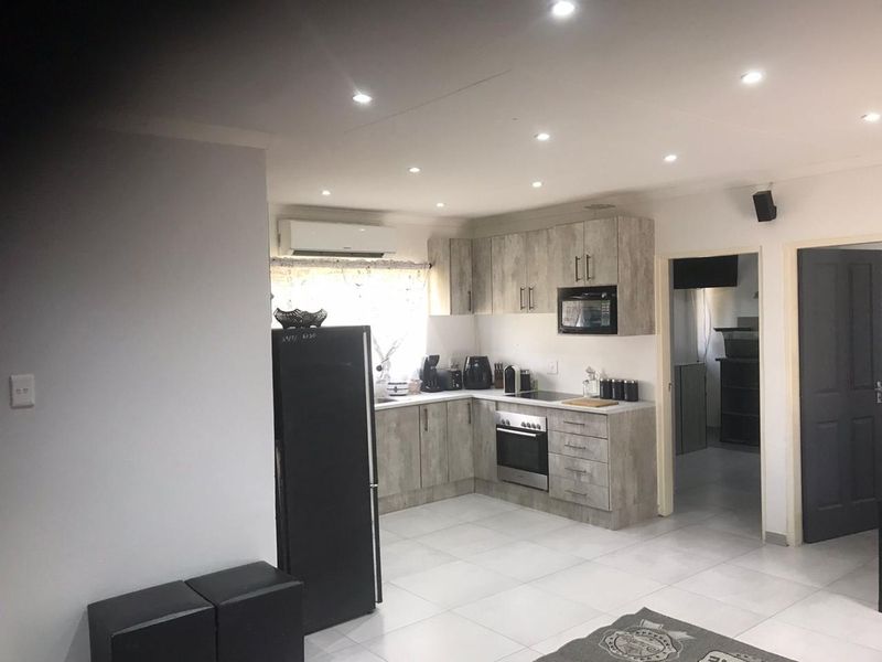 Modern kitchen featuring light wood-grain cabinetry, built-in oven and hob, recessed lighting, and tiled flooring, with an integrated air conditioning unit.