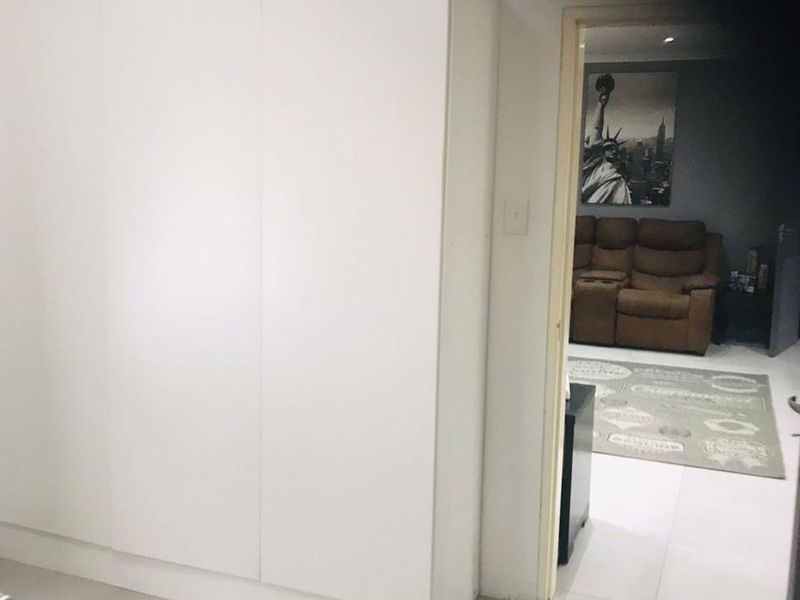 Bedroom featuring white built-in wardrobes and tiled flooring, with a view into an adjacent living area.