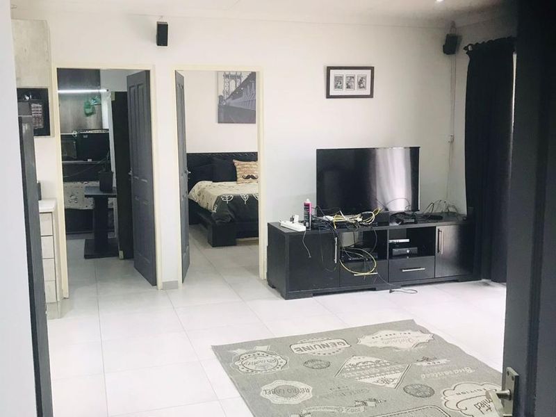 A bright, open-plan living area featuring neutral tiled flooring and recessed downlighting, with direct access to adjacent rooms.