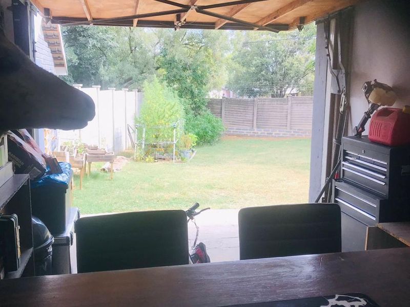 A view from inside a garage looking out towards the rear garden, featuring a manual tilt-up garage door and concrete flooring.