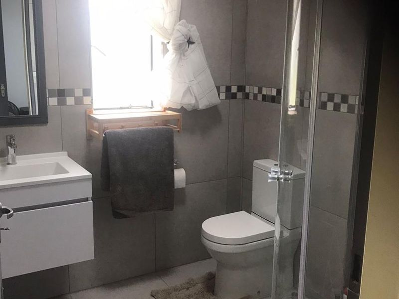 Modern bathroom featuring a wall-mounted vanity, toilet, and a curved glass shower enclosure with neutral grey wall and floor tiling.