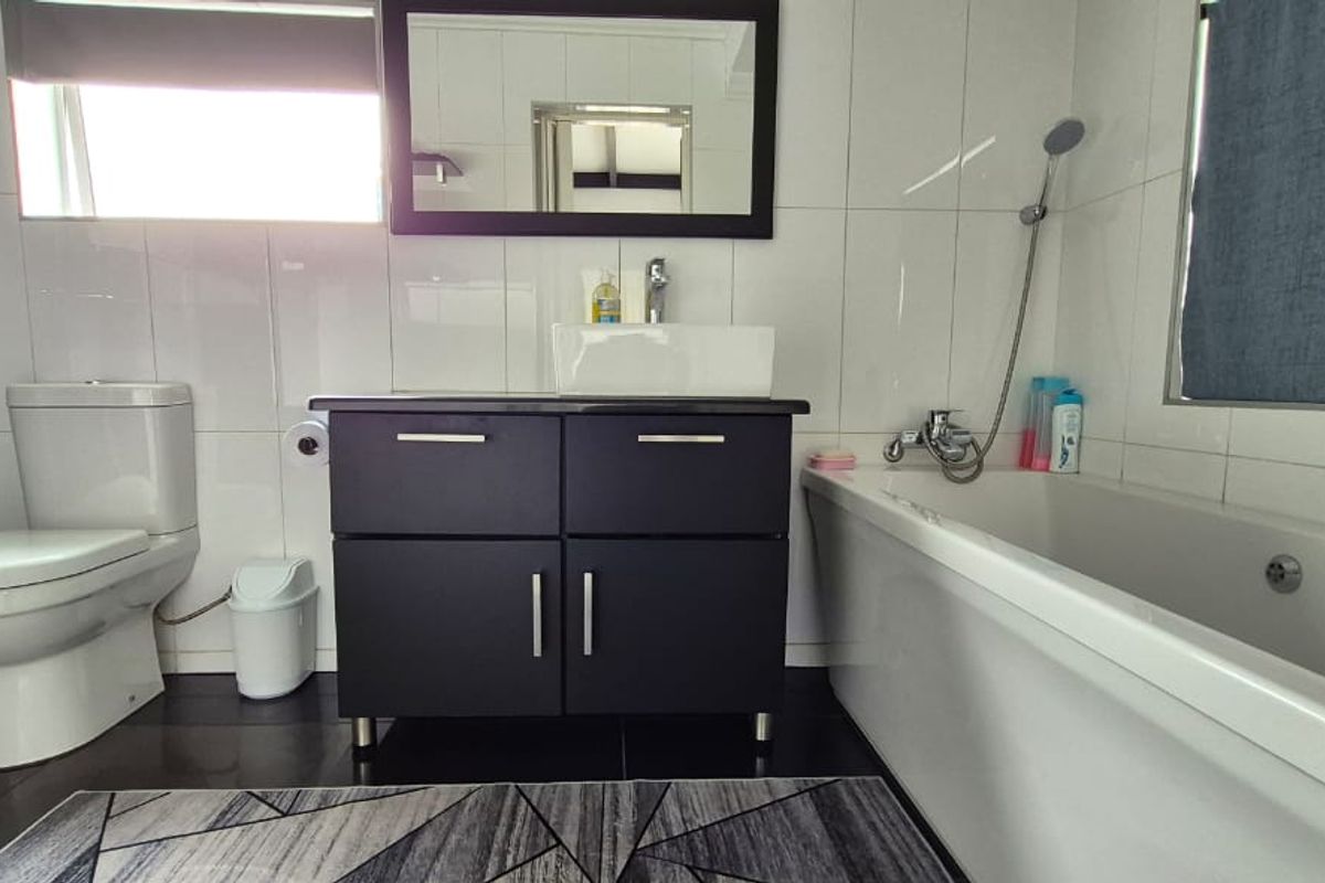 Modern bathroom featuring a dark vanity cabinet, white vessel sink, bathtub with handheld shower attachment, and a separate shower enclosure.